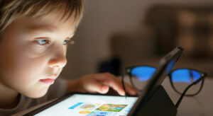 A child looks at a tablet, with a pair of glasses on the table nearby.