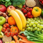 A vibrant, overhead shot showcases a diverse selection of fresh, whole foods arranged on a wooden surface. Colorful fruits like red and green apples, oranges, and yellow bananas mingle with bunches of green grapes. An assortment of vegetables includes green broccoli florets, red, yellow, and green bell peppers, ripe red cherry tomatoes on the vine, and slender cucumbers. Small wooden bowls contain various grains and seeds. The overall impression is one of abundance, health, and the natural goodness of unprocessed ingredients.