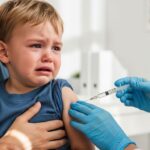 A realistic, close-up photo of a mother gently holding her crying toddler in a doctor's office. A gloved hand, belonging to a doctor, is administering a vaccine with a syringe, with the needle positioned nearly parallel to the child's upper arm. The child has tears on their cheeks and a look of distress, while the mother looks on with a concerned but comforting expression. The background is a clean, bright medical room.
