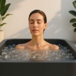 A serene woman with closed eyes meditates in a modern outdoor ice bath, surrounded by ice and minimalist greenery, illustrating the benefits of cold plunge therapy.