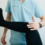 A physical therapist in light blue scrubs carefully assesses a patient's leg and knee joint, demonstrating a crucial step in getting a professional diagnosis for runner's knee.