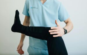 A physical therapist in light blue scrubs carefully assesses a patient's leg and knee joint, demonstrating a crucial step in getting a professional diagnosis for runner's knee.