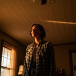 A worried homeowner looks up in a dusty, dimly lit room where sunlight reveals floating particles, symbolizing the unseen hazard of asbestos in your home.
