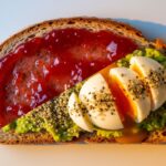 A conceptual top-down shot of sourdough toast split diagonally; the top half is covered in sugary jam representing naked carbs, while the bottom half is topped with avocado, egg, and seeds for protein balance.